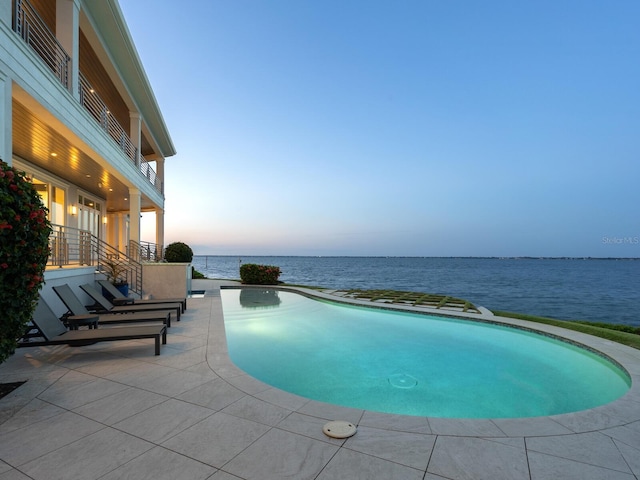 pool at dusk featuring a water view and a patio