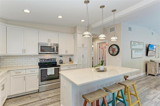 kitchen featuring tasteful backsplash, hanging light fixtures, white cabinets, and stainless steel appliances