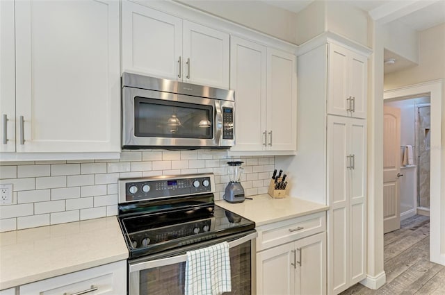 kitchen featuring white cabinets, light wood-type flooring, stainless steel appliances, and backsplash