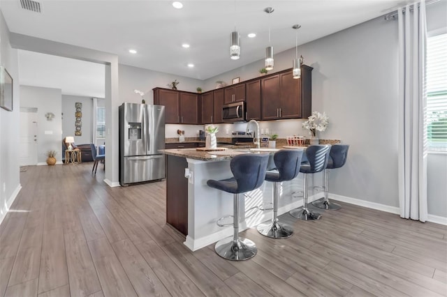 kitchen with a kitchen breakfast bar, light wood-type flooring, dark brown cabinets, stainless steel appliances, and pendant lighting