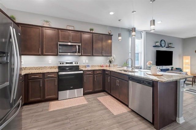 kitchen featuring hanging light fixtures, sink, appliances with stainless steel finishes, light stone counters, and kitchen peninsula