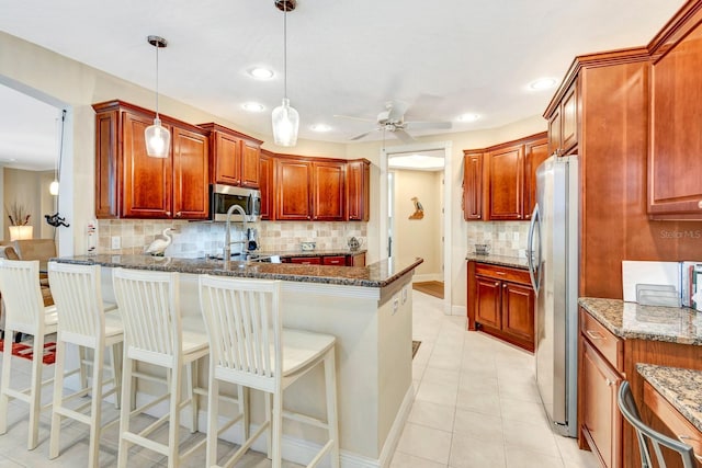 kitchen with dark stone counters, ceiling fan, decorative light fixtures, a kitchen bar, and stainless steel appliances