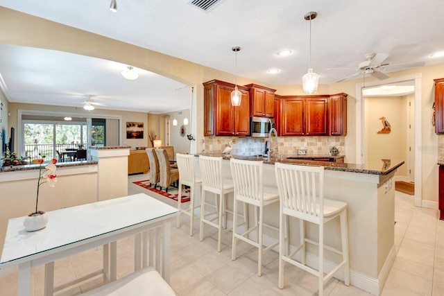 kitchen with backsplash, stone counters, a kitchen breakfast bar, decorative light fixtures, and kitchen peninsula