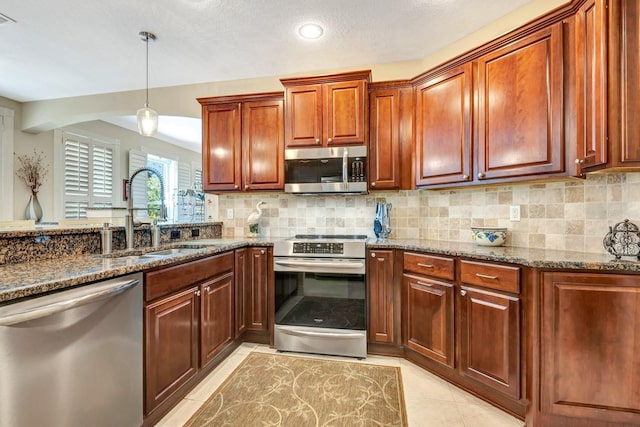 kitchen featuring sink, dark stone countertops, pendant lighting, light tile patterned floors, and appliances with stainless steel finishes