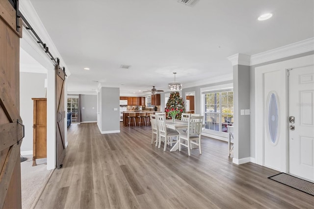 dining room with a barn door, hardwood / wood-style flooring, ceiling fan, and ornamental molding