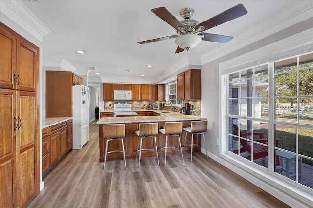 kitchen with sink, kitchen peninsula, white appliances, a breakfast bar area, and ornamental molding