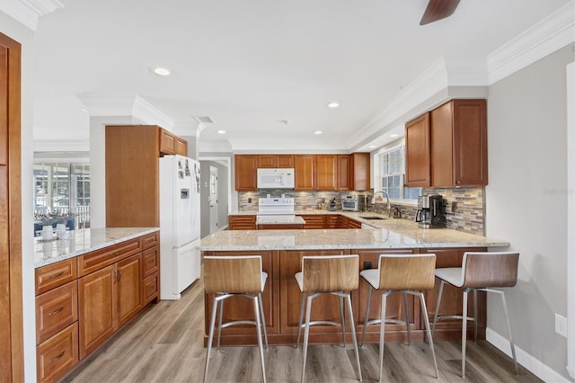 kitchen featuring sink, kitchen peninsula, white appliances, a kitchen bar, and ornamental molding