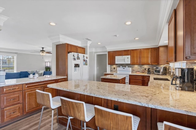 kitchen featuring light stone countertops, sink, a kitchen breakfast bar, kitchen peninsula, and white appliances