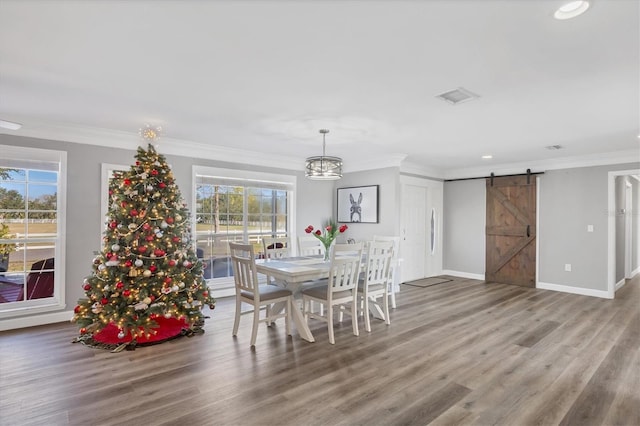 dining space featuring hardwood / wood-style floors, a barn door, ornamental molding, and an inviting chandelier