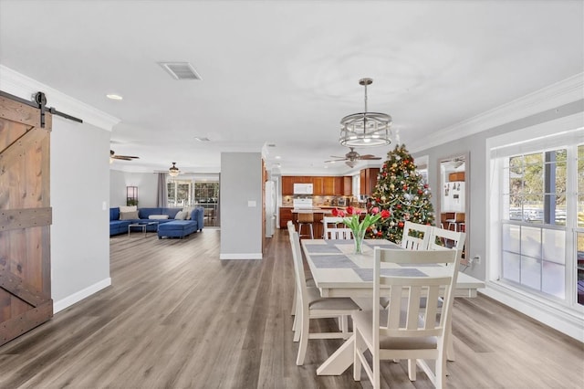 dining space with a barn door, an inviting chandelier, light hardwood / wood-style floors, and ornamental molding