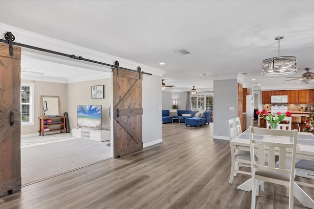 dining space featuring a barn door, hardwood / wood-style flooring, and crown molding