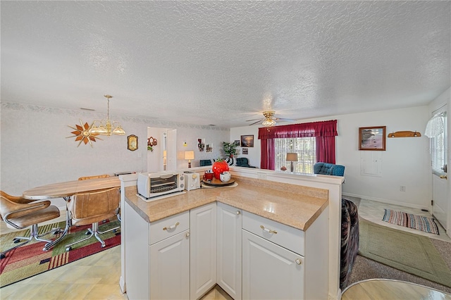 kitchen with a textured ceiling, ceiling fan with notable chandelier, white cabinets, and decorative light fixtures