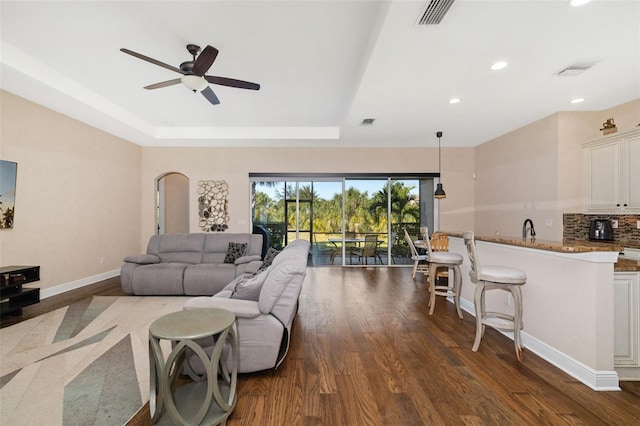 living room featuring dark hardwood / wood-style floors, a raised ceiling, ceiling fan, and sink