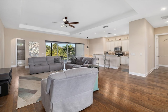 living room with a raised ceiling, ceiling fan, and dark hardwood / wood-style flooring