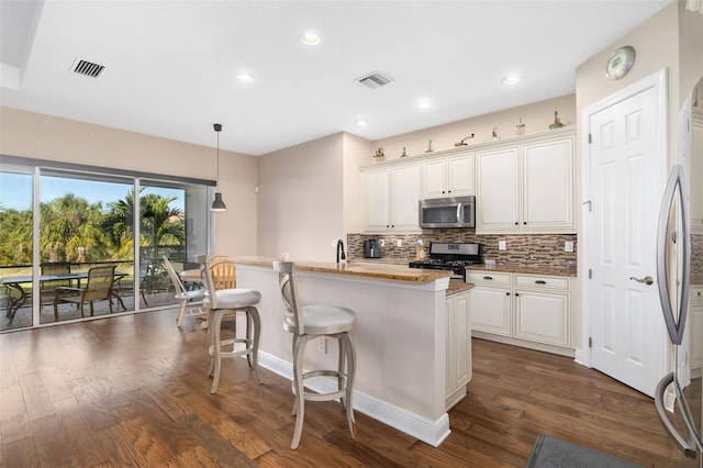 kitchen with white cabinets, a center island with sink, dark hardwood / wood-style floors, appliances with stainless steel finishes, and decorative light fixtures