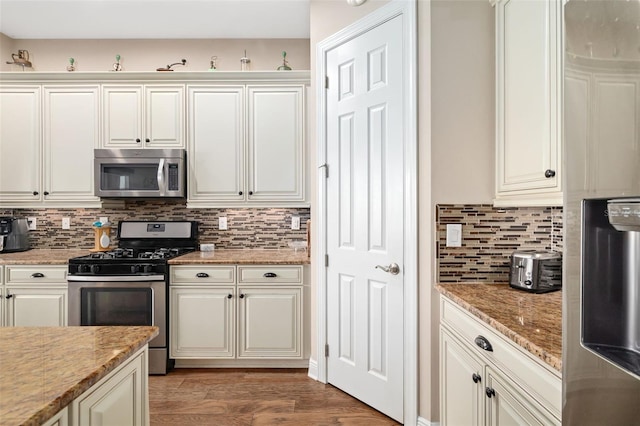 kitchen featuring dark hardwood / wood-style flooring, tasteful backsplash, light stone counters, stainless steel appliances, and white cabinetry