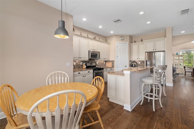 kitchen with light stone countertops, backsplash, pendant lighting, a center island with sink, and appliances with stainless steel finishes