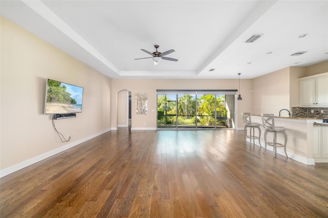 942 Preservation St, Bradenton, FL 34208 - unfurnished living room featuring a tray ceiling, arched walkways, hardwood / wood-style flooring, ceiling fan, and baseboards