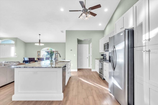 kitchen with light stone counters, stainless steel appliances, sink, a center island with sink, and white cabinets