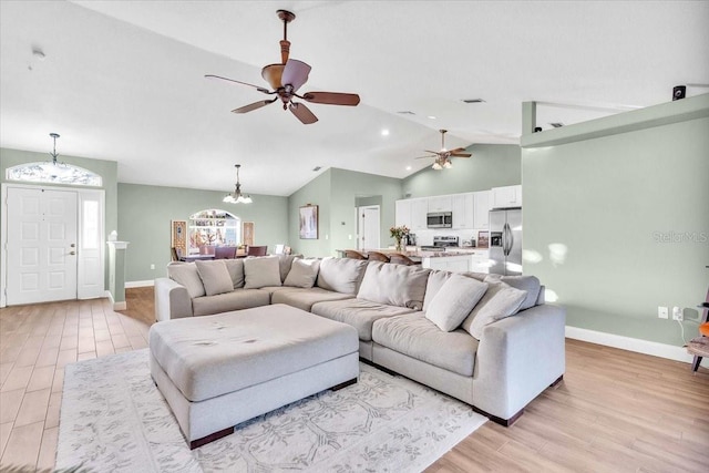 living room with ceiling fan with notable chandelier, lofted ceiling, and light hardwood / wood-style flooring