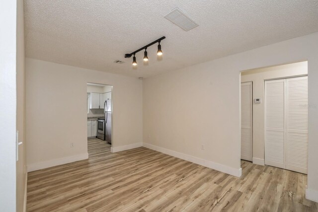 interior space with a textured ceiling, light wood-type flooring, and track lighting