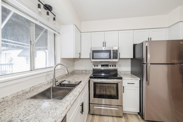 kitchen featuring stainless steel appliances, sink, white cabinetry, light stone counters, and light hardwood / wood-style flooring