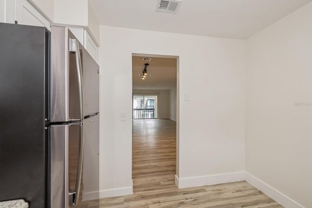 kitchen featuring stainless steel fridge, light hardwood / wood-style floors, and white cabinetry