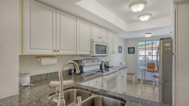 kitchen featuring white cabinetry, sink, dark stone counters, white appliances, and light tile patterned floors