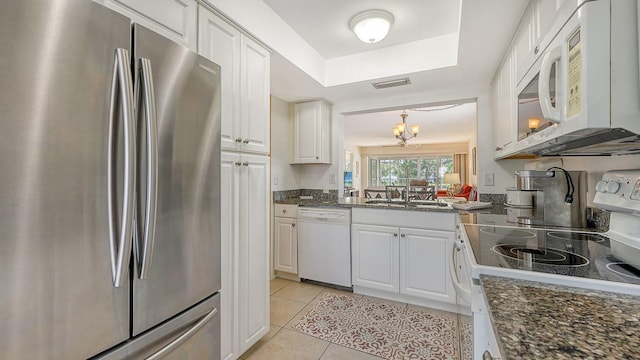 kitchen with white cabinetry, light tile patterned floors, dark stone counters, and white appliances