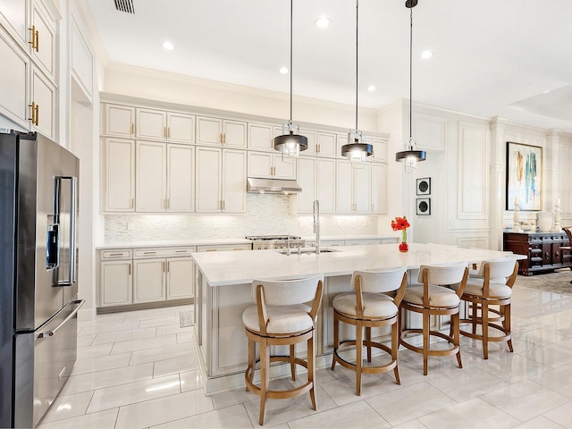 kitchen with pendant lighting, sink, high quality fridge, and an island with sink