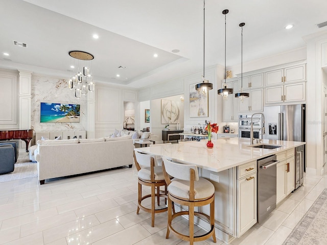 kitchen with hanging light fixtures, a raised ceiling, light stone counters, an island with sink, and a breakfast bar area