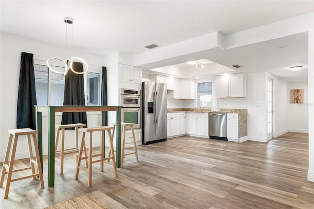 kitchen with appliances with stainless steel finishes, sink, light hardwood / wood-style floors, white cabinetry, and hanging light fixtures