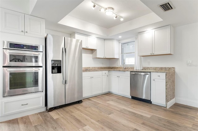 kitchen with light stone countertops, appliances with stainless steel finishes, a tray ceiling, light hardwood / wood-style floors, and white cabinetry