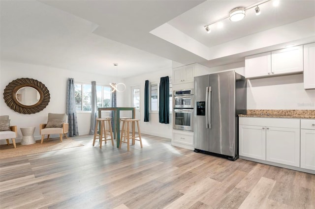 kitchen featuring hanging light fixtures, light hardwood / wood-style flooring, a tray ceiling, white cabinets, and appliances with stainless steel finishes