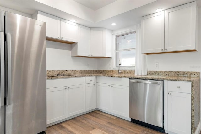 kitchen with white cabinets, light hardwood / wood-style floors, light stone countertops, and stainless steel appliances