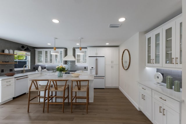 kitchen with pendant lighting, custom exhaust hood, white appliances, backsplash, and a kitchen island