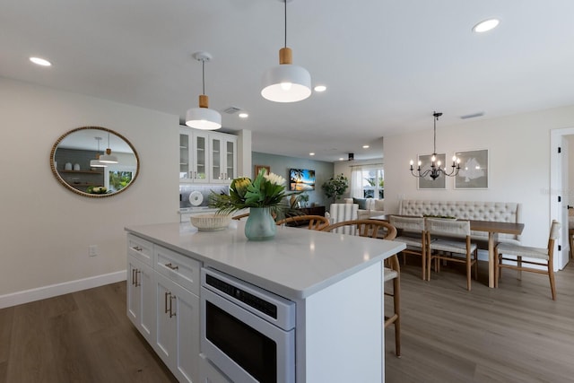 kitchen featuring a kitchen island, built in microwave, decorative light fixtures, hardwood / wood-style floors, and white cabinetry