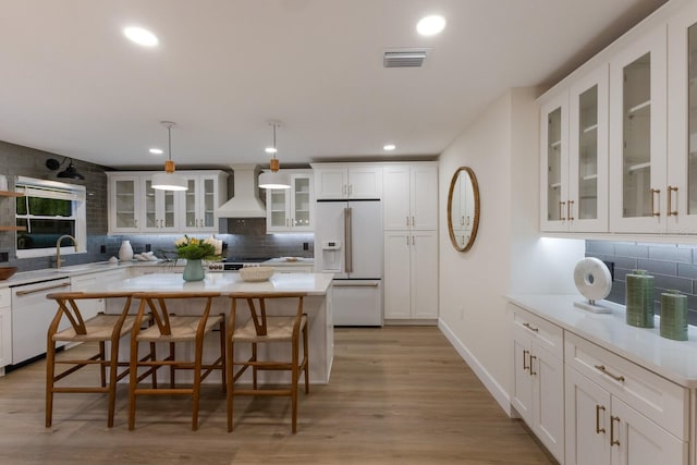 kitchen with white cabinetry, hanging light fixtures, white appliances, decorative backsplash, and custom range hood