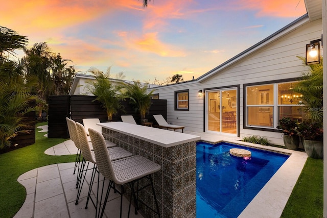 pool at dusk featuring a bar and a patio