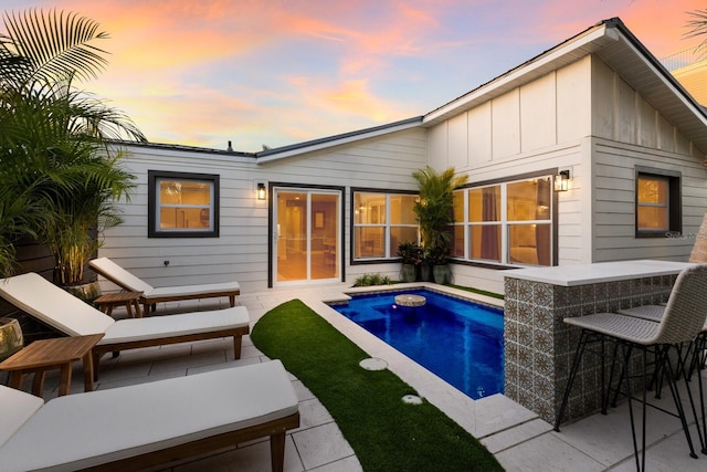 pool at dusk with an outdoor bar and a patio