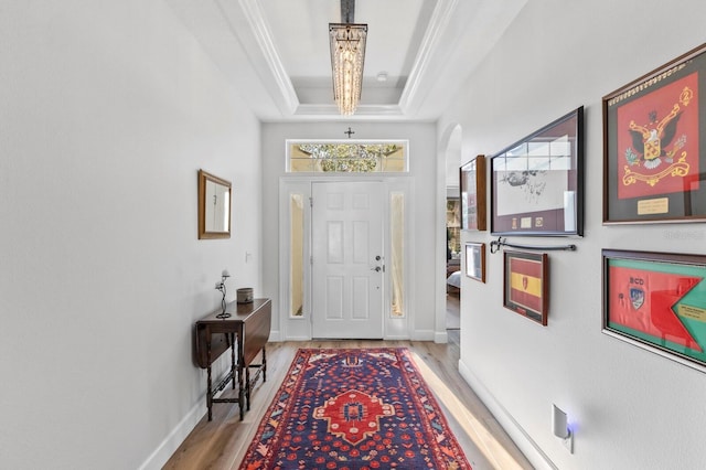 entryway featuring a raised ceiling, ornamental molding, and light wood-type flooring