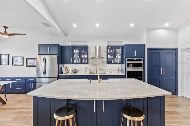 kitchen with a large island with sink, wall chimney range hood, stainless steel appliances, and a breakfast bar area