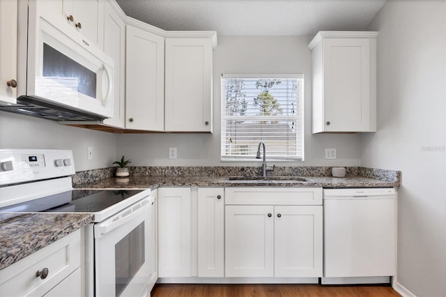 kitchen featuring white appliances, white cabinetry, dark stone countertops, and sink