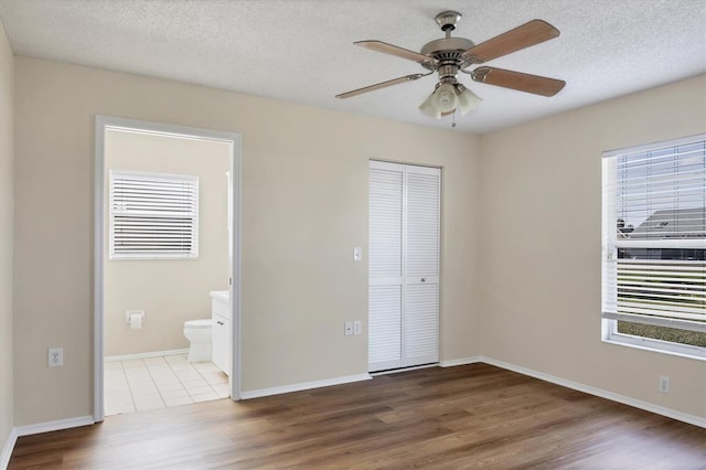 unfurnished bedroom with ensuite bathroom, hardwood / wood-style flooring, ceiling fan, multiple windows, and a closet