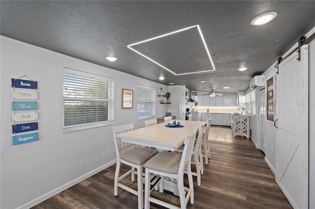 dining area featuring a barn door, dark hardwood / wood-style floors, a wall unit AC, and ceiling fan