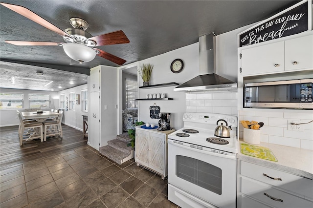 kitchen with white range with electric cooktop, stainless steel microwave, white cabinets, and wall chimney range hood