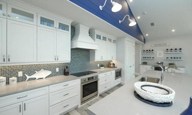 kitchen with premium range hood, appliances with stainless steel finishes, white cabinetry, sink, and backsplash