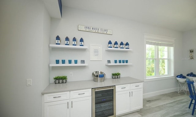 bar with wine cooler, white cabinetry, and light hardwood / wood-style flooring