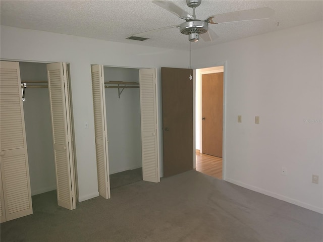 unfurnished bedroom featuring ceiling fan, carpet floors, a textured ceiling, and two closets