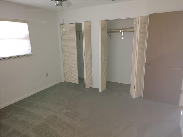 unfurnished bedroom featuring carpet flooring, ceiling fan, and two closets